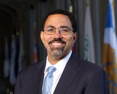 SUNY Chancellor John B King headshot in front of SUNY flags