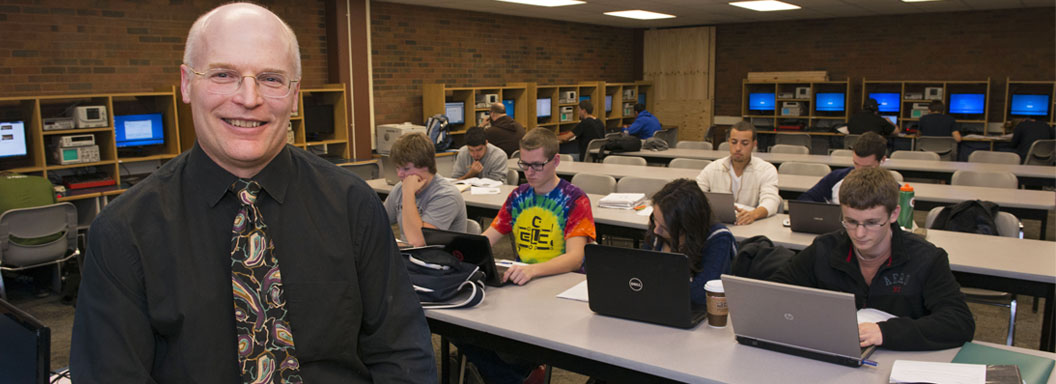 John Wadach, Professor of science, engineering, and physics at Monroe Community College, smiling in front of his classroom.